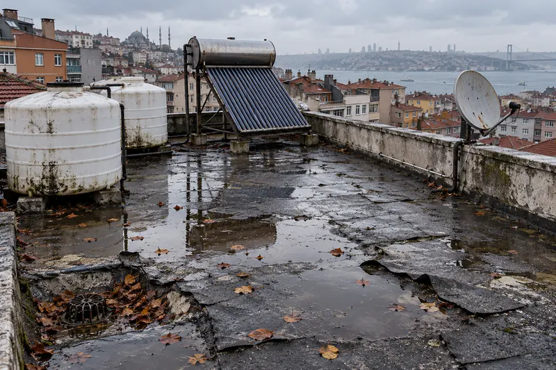 Çatlamış eski membranlı terasta yağmur sonrası su birikintileri ve yapraklar